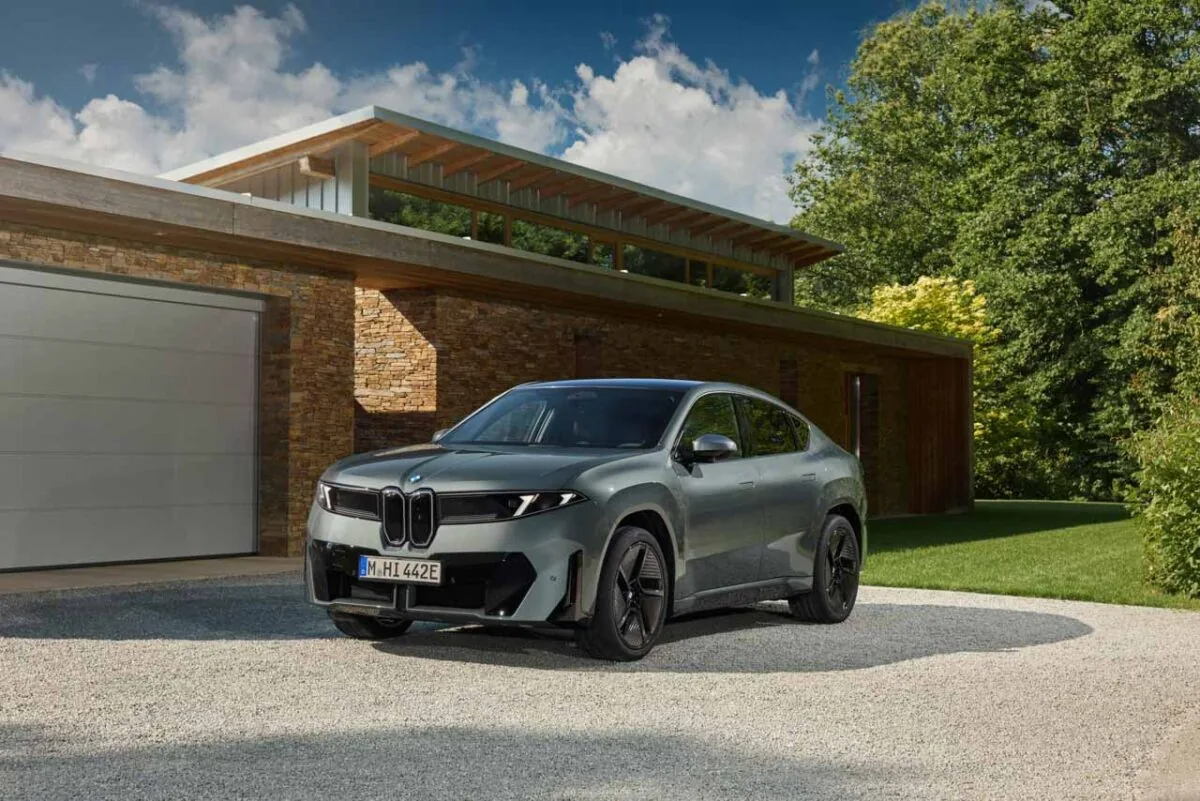 نمای سه‌رخ جلوی شاسی‌بلند برقی BMW iX4 نقره‌ای با جلوپنجره دوگانه، چراغ‌های LED باریک و سقف کوپه در مقابل خانه‌ای مدرن