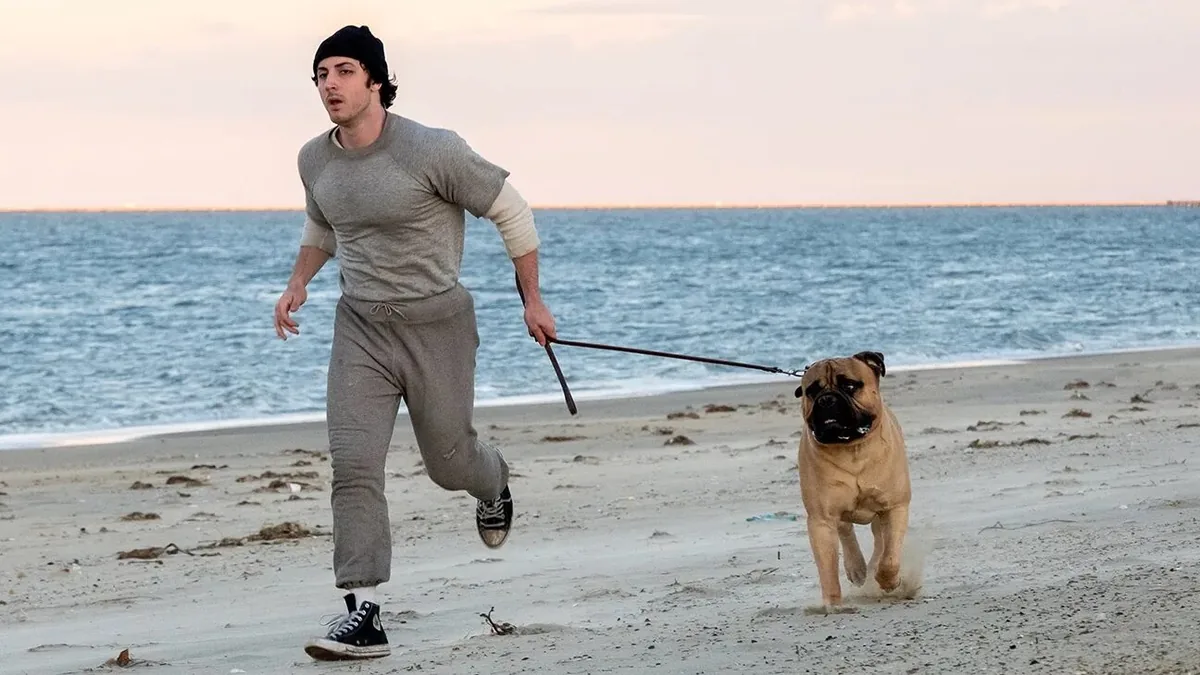 Man Jogging on a Sandy Beach While Holding a Leash Attached to a Brown Dog