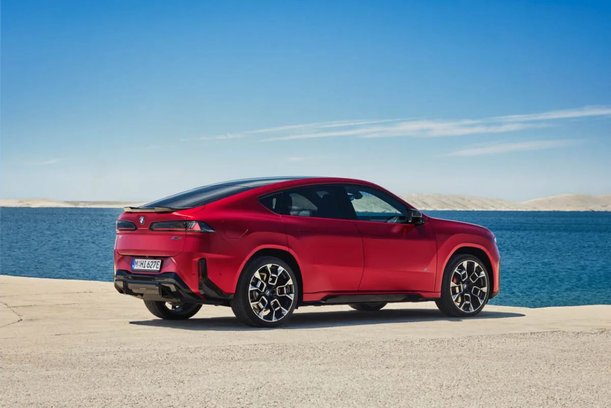 نمای سه‌رخ عقب خودروی برقی BMW iX4 M60 قرمزرنگ در کنار دریا، با سقف شیب‌دار، چراغ‌های کشیده عقب و رینگ‌های اسپرت
