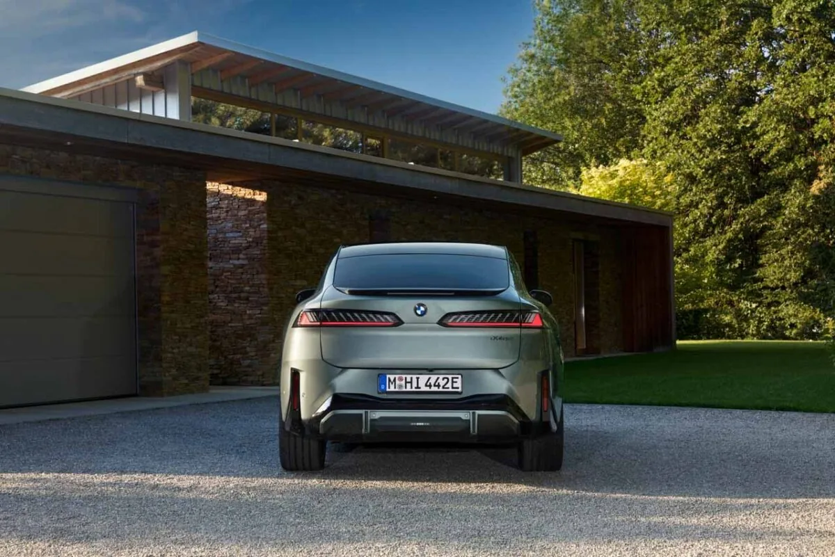 نمای مستقیم عقب BMW iX4 نقره‌ای با چراغ‌های LED افقی، نشان BMW و سپر مشکی در محوطه خانه‌ای مدرن
